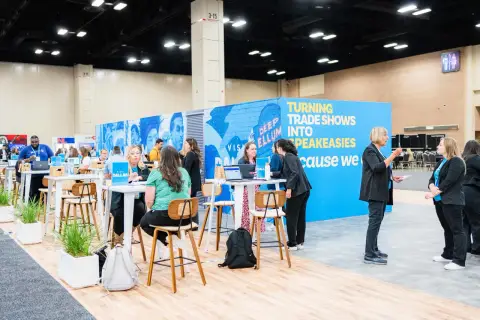Attendees network at government trade shows, with a vibrant blue booth promoting "Turning Trade Shows Into Speakeasies.